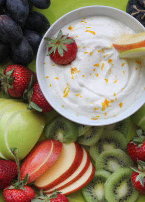yogurt fruit dip in bowl surrounded by colorful slices of kiwis, apples, strawberries, and grapes